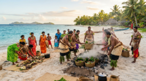 On a sandy beach in Fiji at sunset, a group of Fijian men in traditional tapa cloth and garlands use poles to lift woven baskets of food from a steaming earth oven pit. Other villagers, including women and children in colorful dresses and traditional attire, watch or prepare food on woven mats nearby. Palm trees, traditional bures, and distant islands are visible in the background under a warm sky.